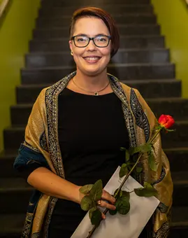 Ein Foto von Dr. Mareike Spychala, eine wei?e Frau mit kurzen Haaren, Sidecut und Brille. Sie tr?gt ein schwarzes Kleid und steht vor einer Treppe.