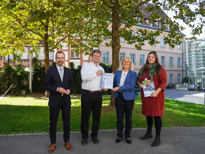 Universit?tspr?sident Kai Fischbach, Frank Lechner, Leiter des Referats Umwelt/Energie der IHK fr Oberfranken Bayreuth, Universit?tskanzlerin Dagmar Steuer-Flieser, nd Carolin Brix-Asala, Umweltmanagementbeauftragte der Universit?t, stehen vor einem Baum im Burgershof. 