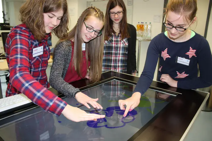 M?dchen stehen um einen Tisch und begeistern sich beim Girls' Day fr Technik.